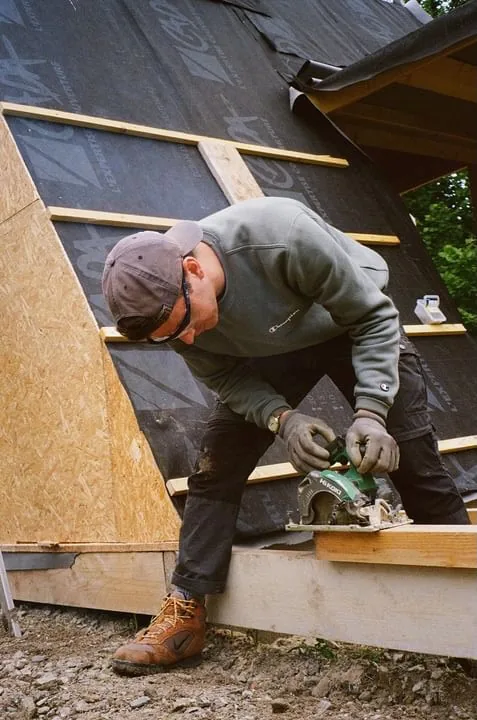 Erwan fixing roof panels on a wooden A-frame cabin